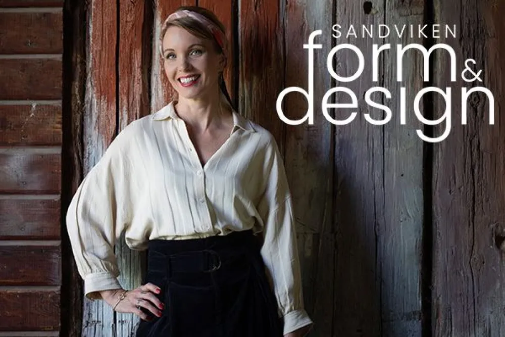 Porträttfoto på Erika Åberg, som står leendes mot en gammal byggnadsvägg. Bredvid finns en monterad logga som säger "Sandviken form&design"