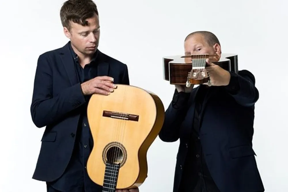 Två män inspekterar en varsin gitarr. 